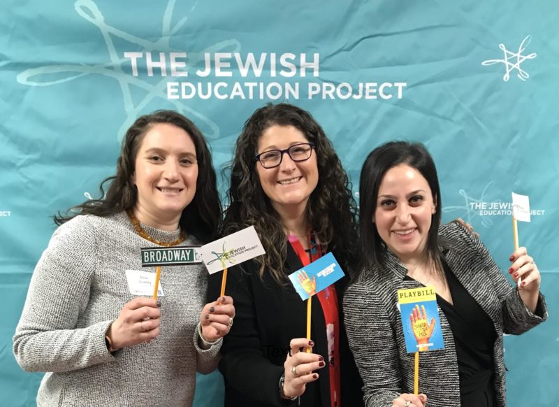 Three Teen Educators against a turquoise backdrop with the TJEP logo, holding up little signs that say Broadway and little Playbills