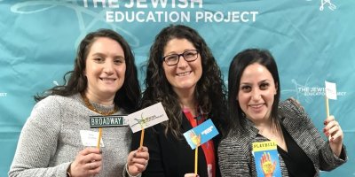 Three Teen Educators against a turquoise backdrop with the TJEP logo, holding up little signs that say Broadway and little Playbills