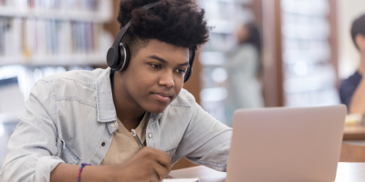A teenage boy is learning with headphones on in front of a screen