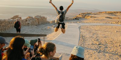 A teen jumping with their fists in the air overlooking desert cliffs
