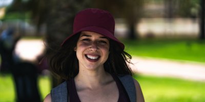 Woman in black tank top and maroon bucket hat with backpack straps smiling outdoors