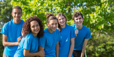 A group of teens in matching blue t-shirts huddled together smiling outdoors