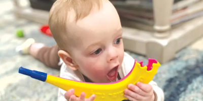 An infant is lying on the floor holding a plastic Shofar