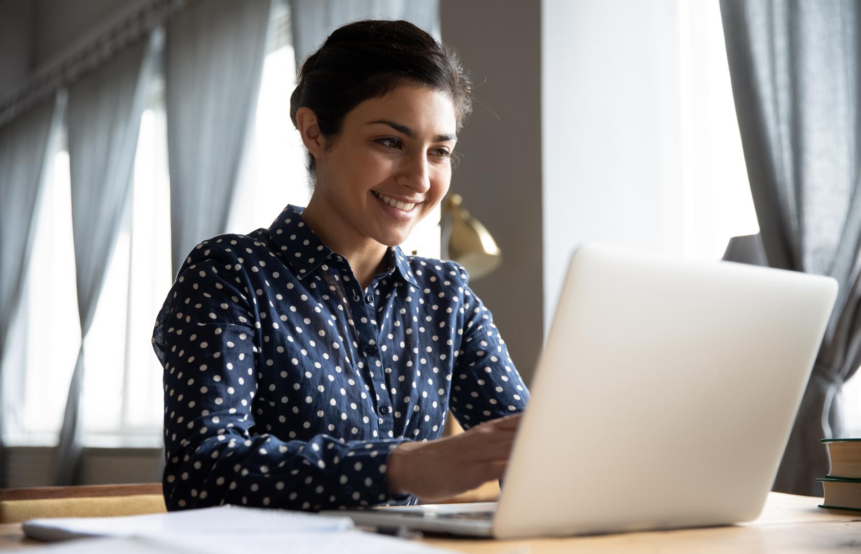 A woman sits with her laptop, smiling