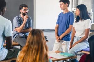 A teacher huddles around his teenage students in serious conversation