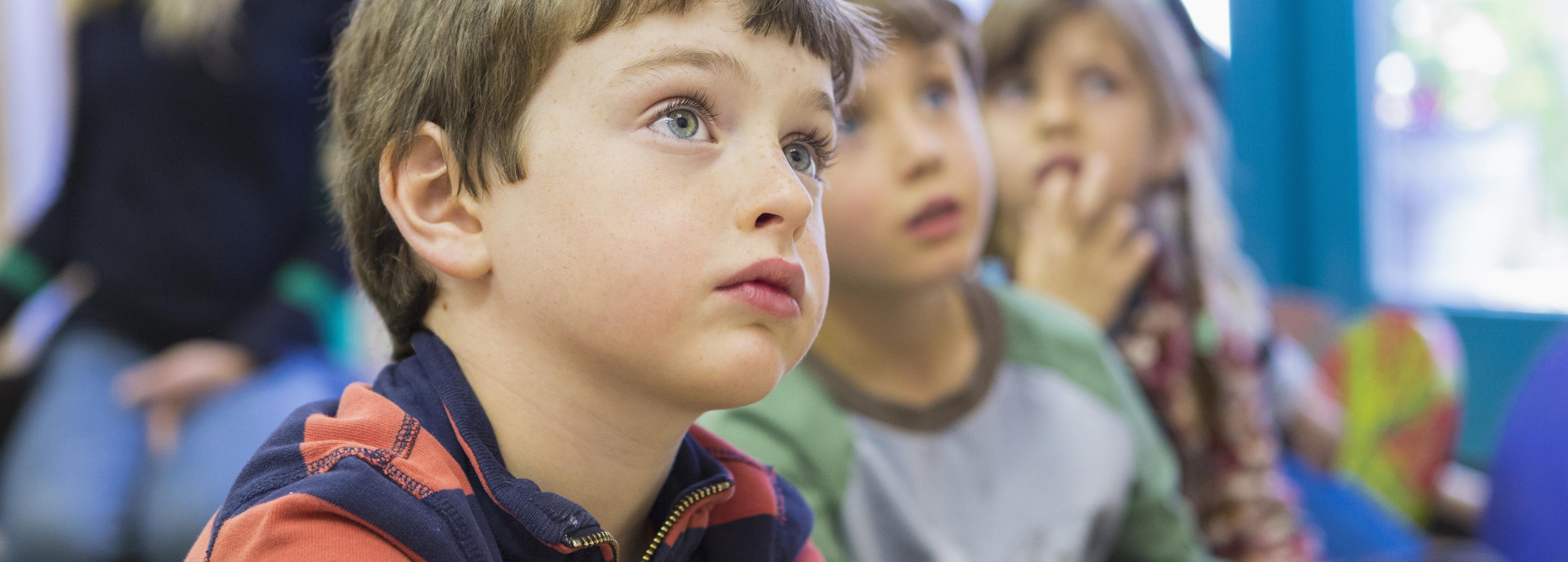 Young children in a classroom look up, possibly at their teacher