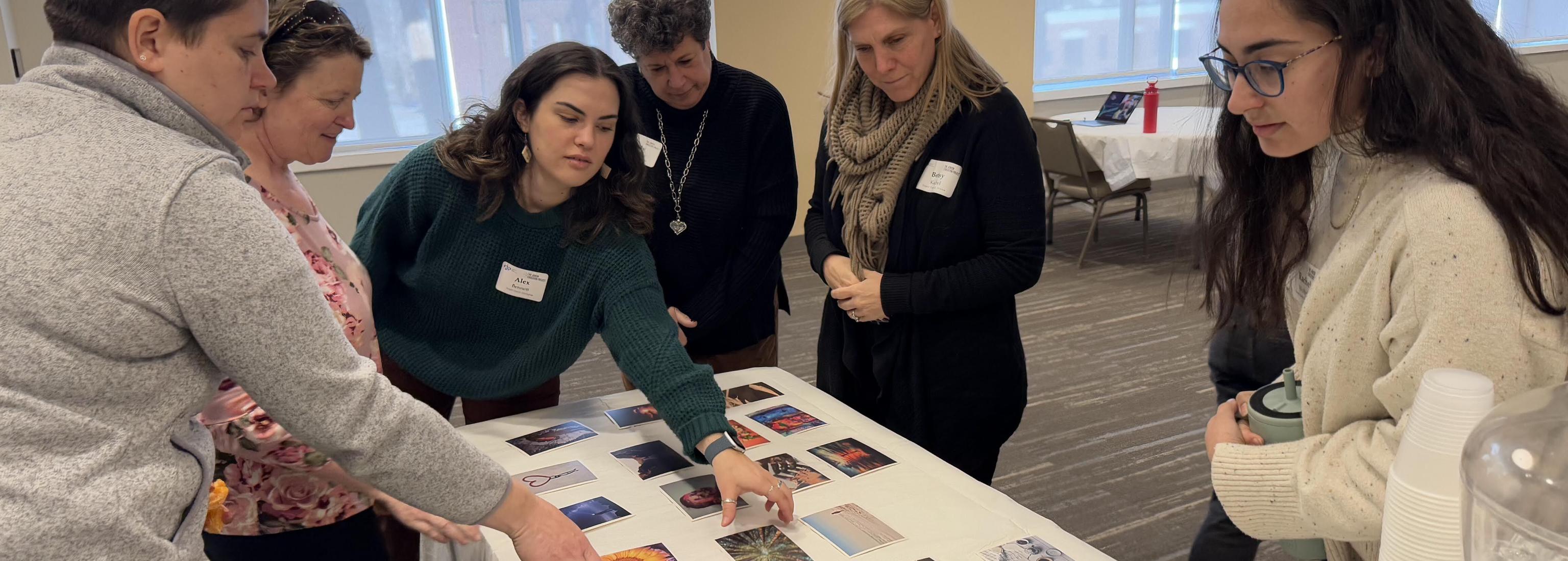 A group of female educators stand over a table with photos spread out and two of them select photos