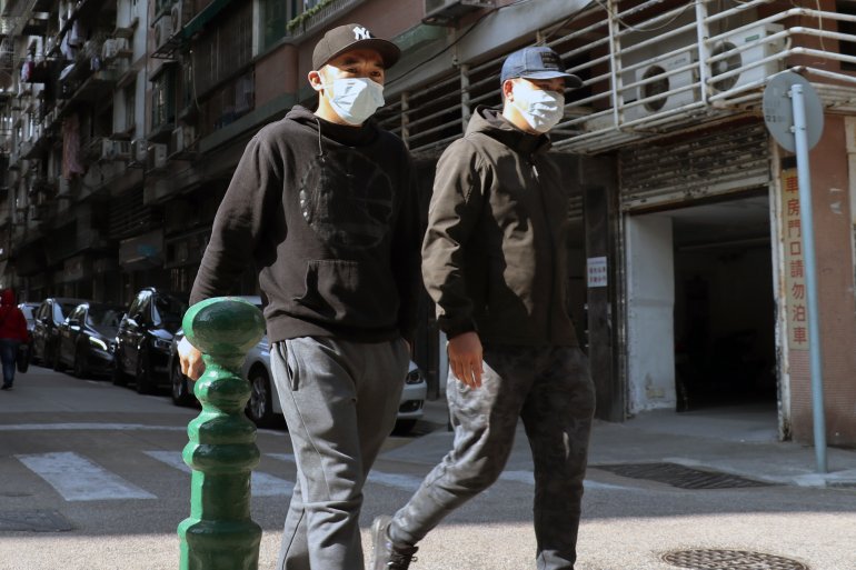 Two men walk down a street wearing protective masks 