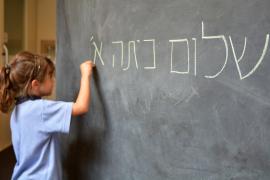 A young girl writes in Hebrew on a chalkboard