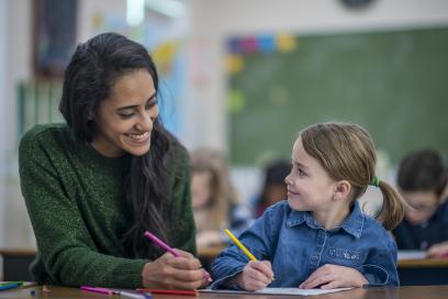 A teacher smiling with her student who is a young girl in a classroom
