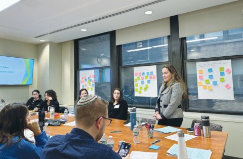 An educator standing before a room of educators at a table