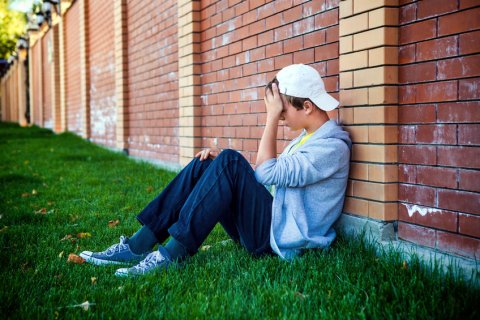 Sad teenage boy sitting against a wall