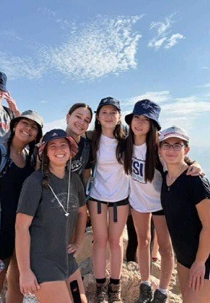 A group of teens on top of a mountain with sky in the background