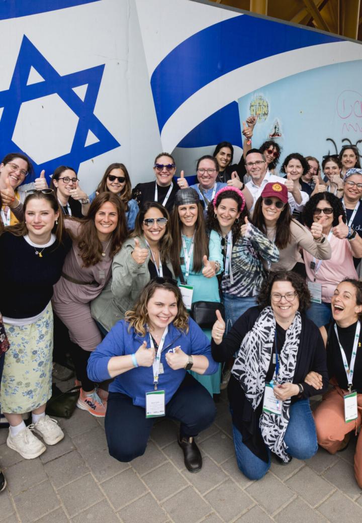 a group of educators stand and pose in front of Israeli flag