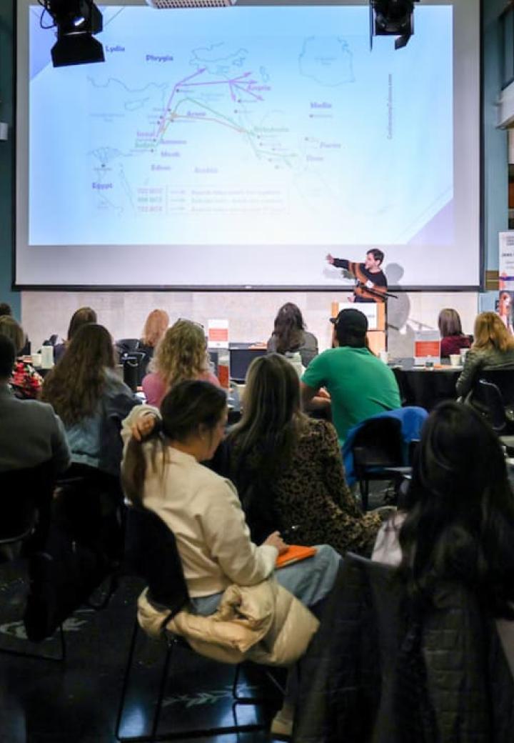 A crowd looks at a speaker and his presentation