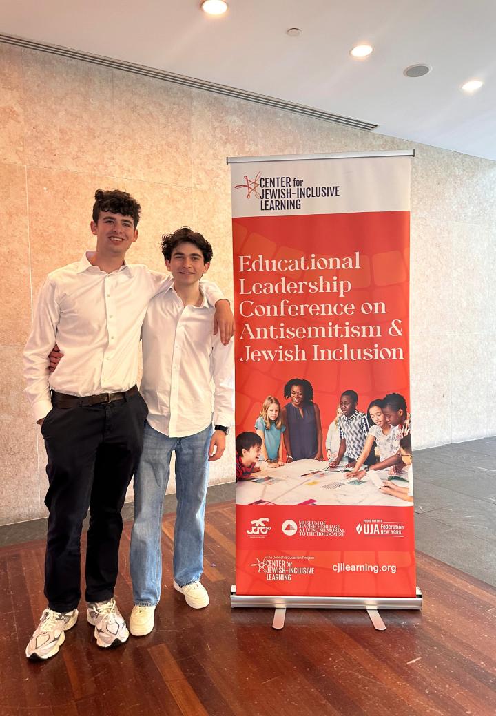 two teen boys stand next to a CJIL banner