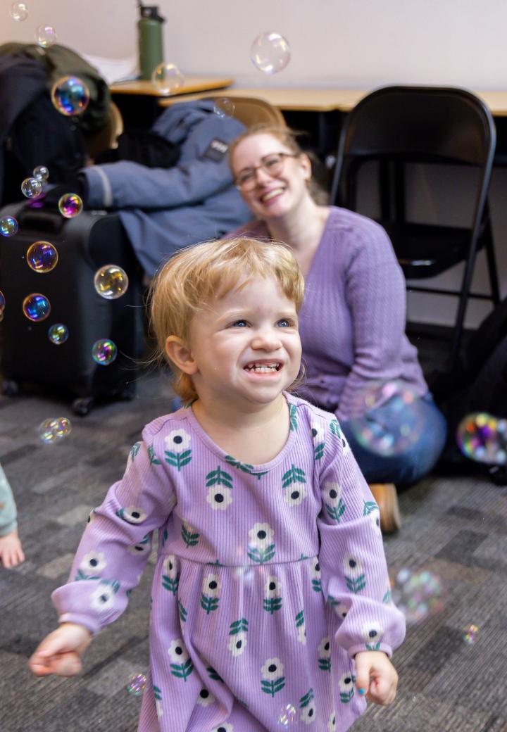 a little girl in a purple dress plays with bubbles