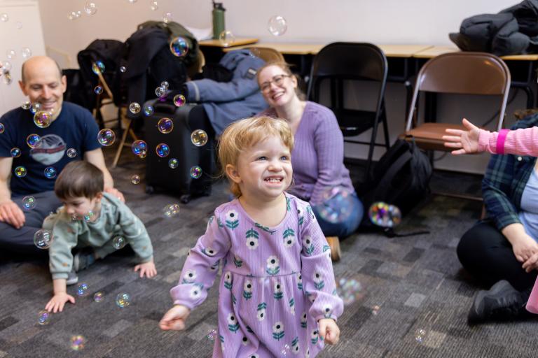 a little girl in a purple dress plays with bubbles