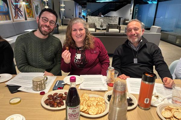 Two men and a woman sit posing at a table - one is holding a date
