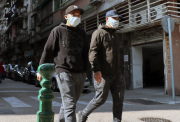 Two men walk down the street wearing protective masks